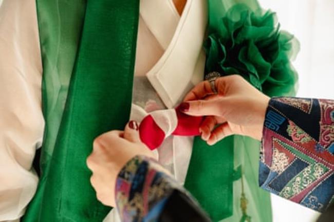 Hands tie a red bow on a traditional white and green hanbok.